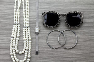 Accessori vari donna sui toni del grigio argento. Collana di perle, orologio, orecchini ad anello e occhiali da sole