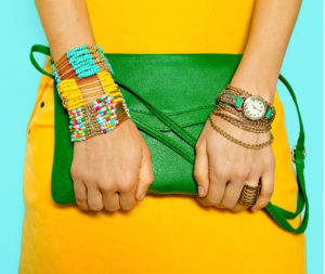 Particolare di polsi e mani di una ragazza bigiotteria etnica molto vistosa e mini bag verde smeraldo su abito giallo vivo