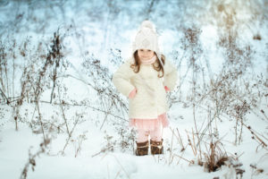 Bimba nella neve con piumino e cappello bianco e vestitino rosa con volant