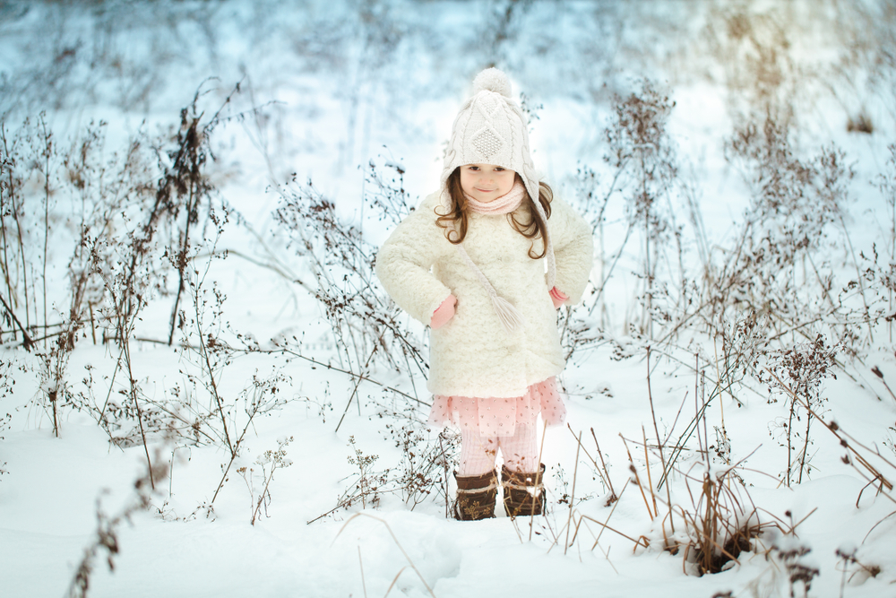 Bimba nella neve con piumino e cappello bianco e vestitino rosa con volant