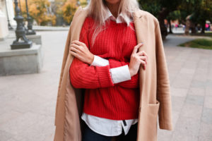 Ragazza che indossa una camicia bianca abbinata ad un maglione rosso e cappotto beige