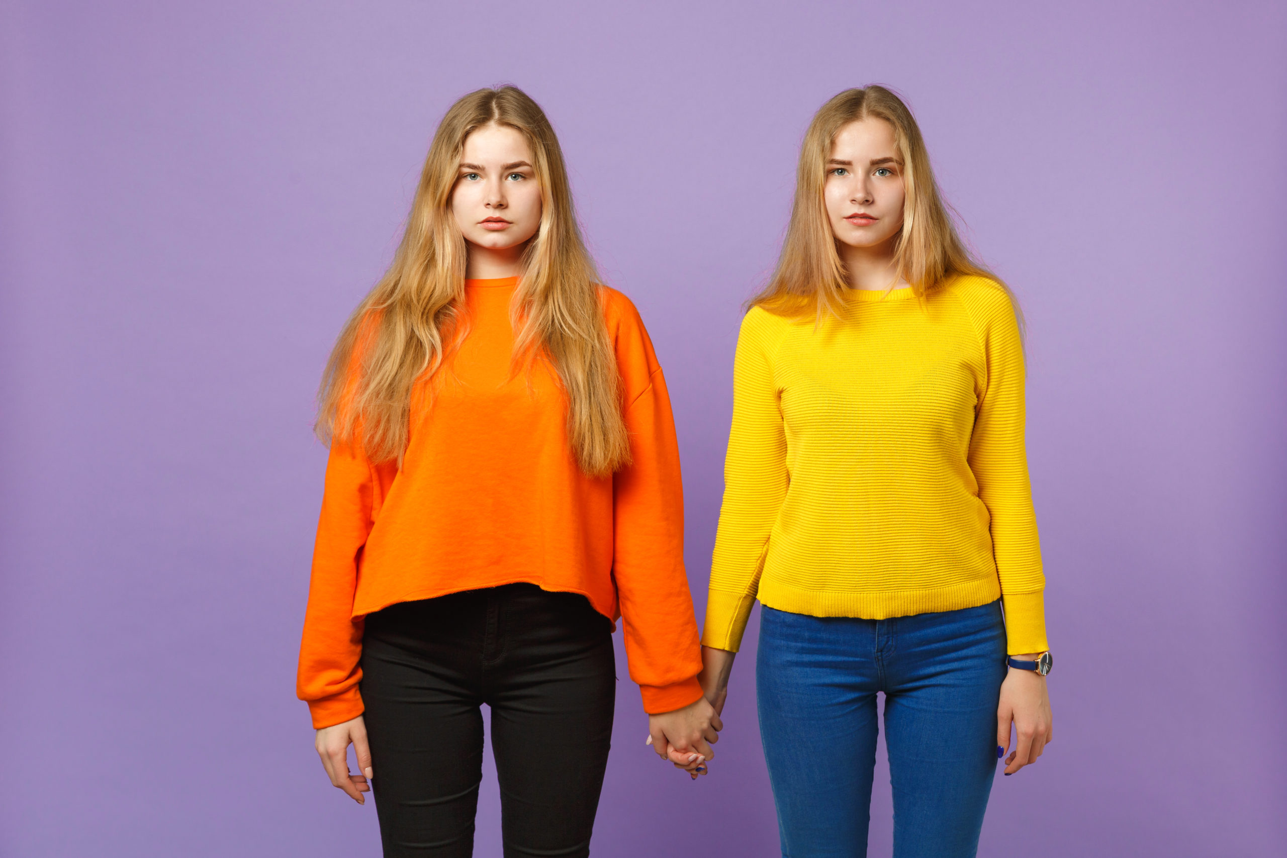 Coppia di ragazze che indossano accostamenti di due colori. Pantaloni neri e maglioncino arancio e pantaloni jeans blu e maglioncino giallo