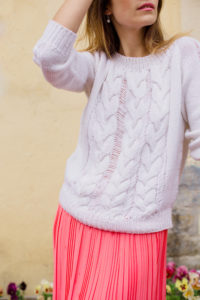 Ragazza che indossa un maxi pull in lana bianca a trecce abbinato ad una gonna plissettata rosa shocking