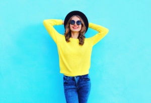 Ragazza che indossa jenas blu e pull giallo lime abbinati a cappello nero e occhiali da sole