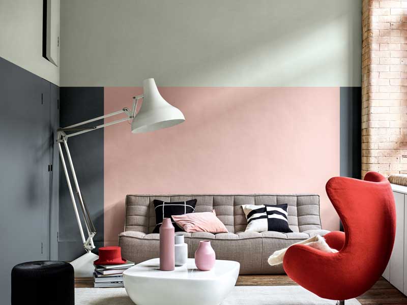 Ambiente casa con divano e poltrona nelle tinte del grigio e rosso. Pareti rosa e grigio scuro.. Complementi vari come pouf, tavolinetto e vasi